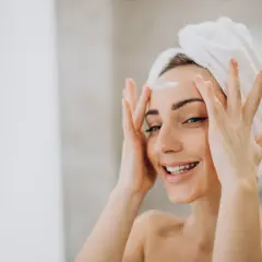 Kobieta z ręcznikiem na głowie nakłada krem na czoło.